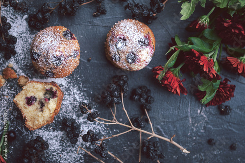 muffin with currants on a dark background next to the berries on the branches. and a bouquet of flowers. in a rustic style. dark style