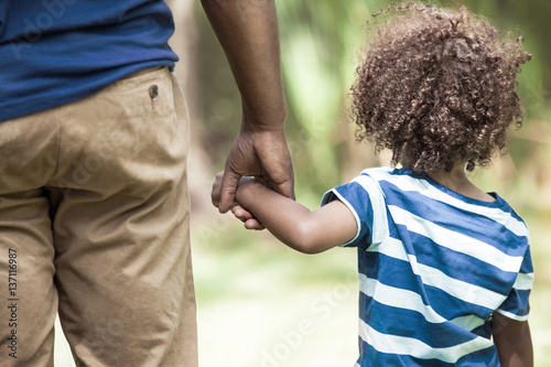 Rear view of girl (2-3) holding hands with her father in field