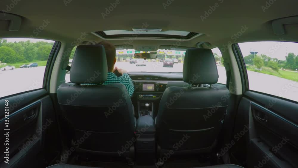 View from the backseat as a man drives through a toll, in 4K. View from the backseat as a man drives through a toll, in 4K.