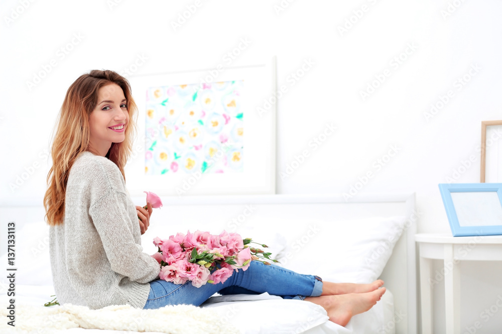 Happy young woman with beautiful bouquet of eustoma flowers sitting on bed at home