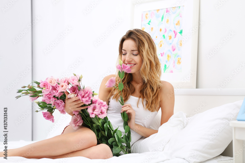 Young cheerful woman with beautiful bouquet of eustoma flowers lying on bed at home Young cheerful woman with beautiful bouquet of eustoma flowers lying on bed at home