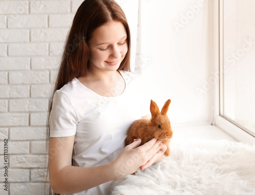 Beautiful girl holding small rabbit on windowsill © Africa Studio