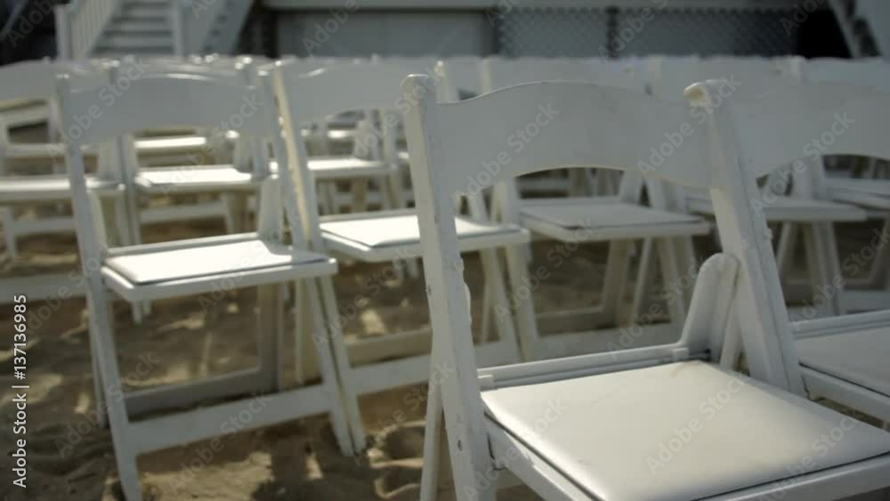 White chairs set up on a beach for a wedding ceremony