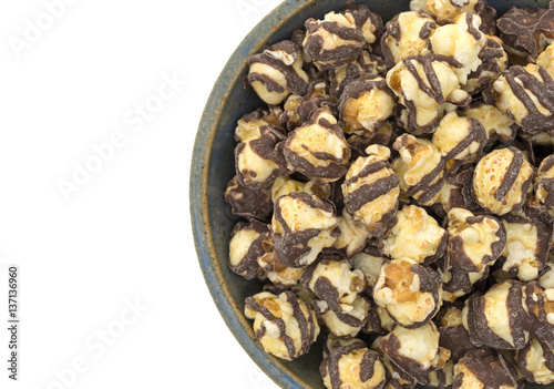 Top close view of fudge drizzled popcorn in an old stoneware bowl isolated on a white background.