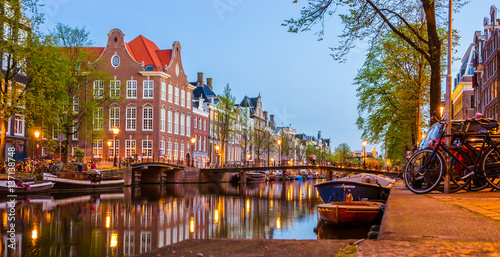 Photography Traditional old buildings and boats at night in Amsterdam, Netherlands