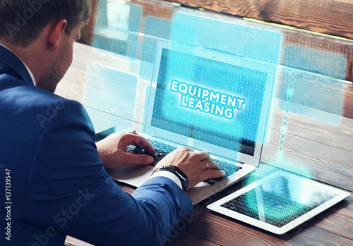 Business, technology, internet and networking concept. Young businessman working on his laptop in the office, select the icon Equipment leasing on the virtual display.