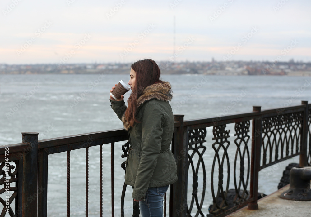 Depressed young woman drinking coffee on pier Depressed young woman drinking coffee on pier