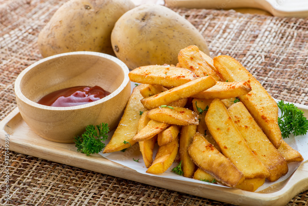 Tasty french fries on cutting board with ketchup, on wooden table background Tasty french fries on cutting board with ketchup, on wooden table background