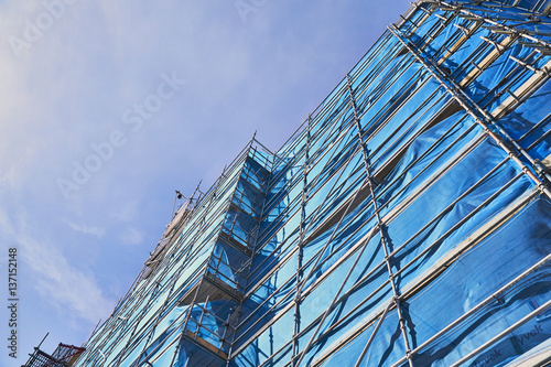 Scaffolding and blue mesh around a new building construction against a blue sky