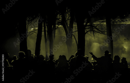 People gathered in a forest looking at a spaceship at night.
