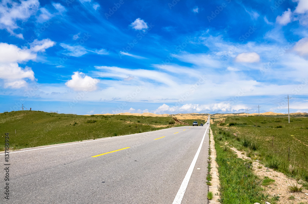 Road on grassland with sunny blue sky and white clouds