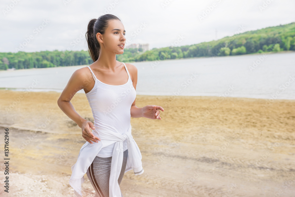 Portrait of beautiful athletic brunette female runner jogging in city park and lake. Healthy fitness woman jogging outdoors. Nature background. Motivation sport. Portrait of beautiful athletic brunette female runner jogging in city park and lake. Healthy fitness woman jogging outdoors. Nature background. Motivation sport.