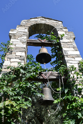 Two bells hanging on wooden beams in the stone arch among green plants