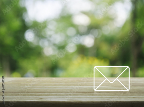 Mail icon on wooden table over blur green tree in garden, Contact us concept