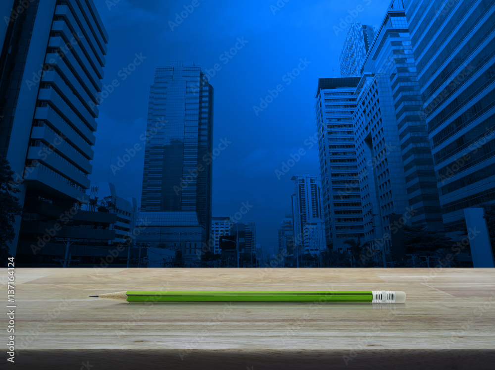 Green pencil on wooden table over modern office city tower, Business concept and idea