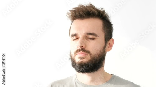 Closeup of young happy bearded man opening his closed eyes, smiling and enjoying sunlight, isolated on white background.