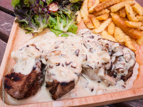 Close up steak pork with mushroom sauce, french fries and salad on wood plate.