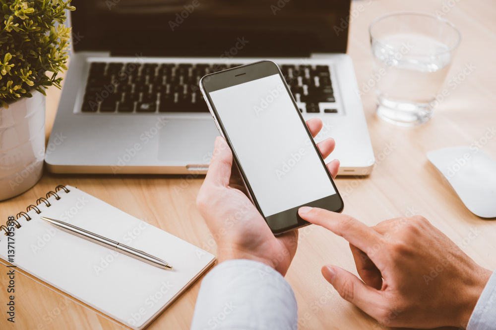 Businessman hand holding a phone with isolated screen over the desk in the office Businessman hand holding a phone with isolated screen over the desk in the office