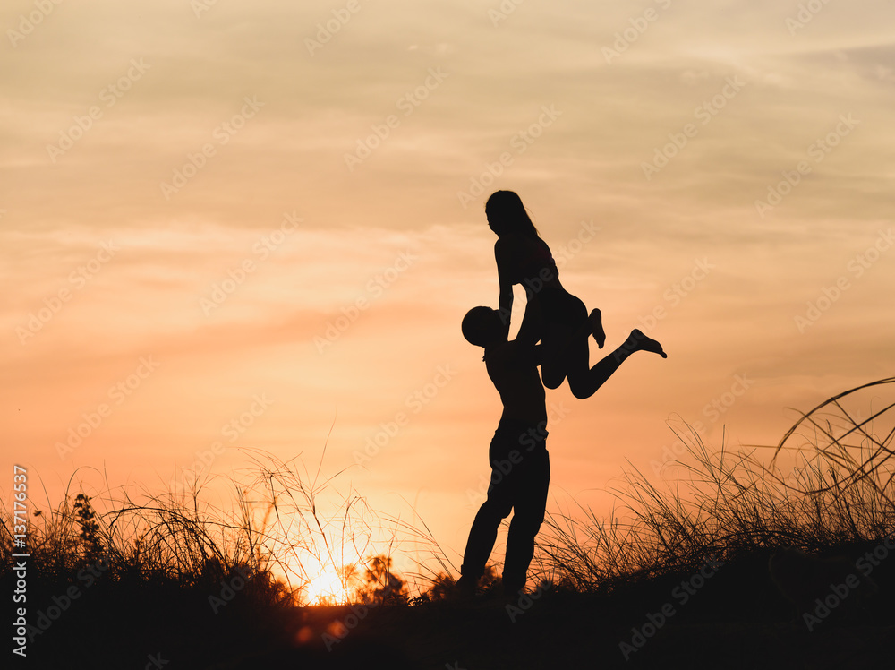 Silhouette happy guy holding his girlfriend while the latter raising her arms at sunset