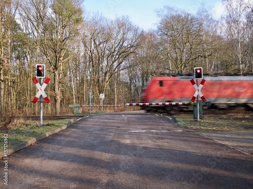 Obraz na plátně Red train speeding through a level crossing