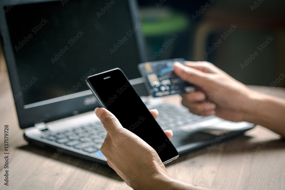 Hand holding smart phone and credit card for shopping online with laptop Hand holding smart phone and credit card for shopping online with laptop
