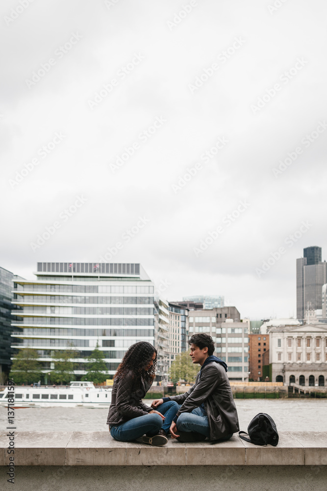 Multi-ethnic couple sitting in the River Thames pier Multi-ethnic couple sitting in the River Thames pier