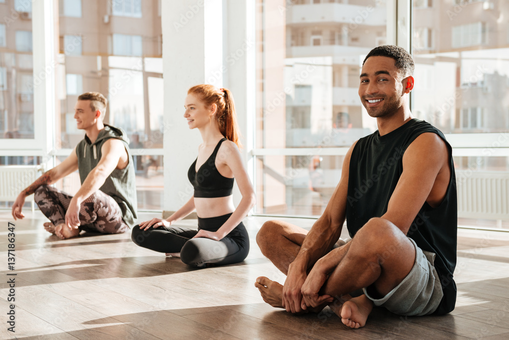 Happy african young man sitting and doing yoga in group