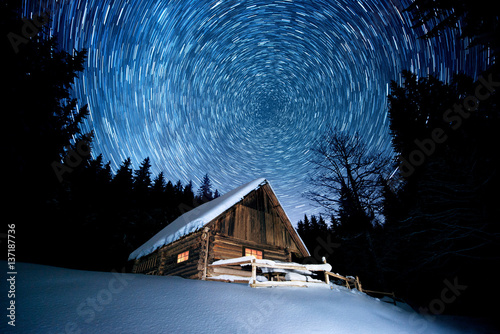 Star trails over wooden house in the winter forest