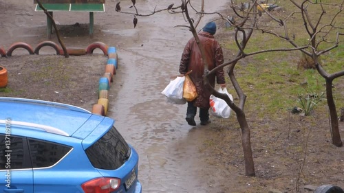 The woman tramp in the rain goes in search of food next to the dumpster photo