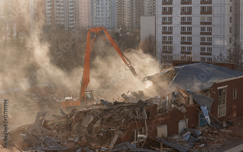 Excavator demolition in sunlit dust cloud dismantles the building in residential area photo