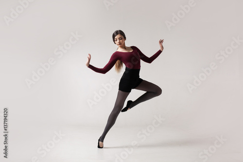 young beautiful woman dancer with long brown hair wearing maroon swimsuit posing on a light grey studio background