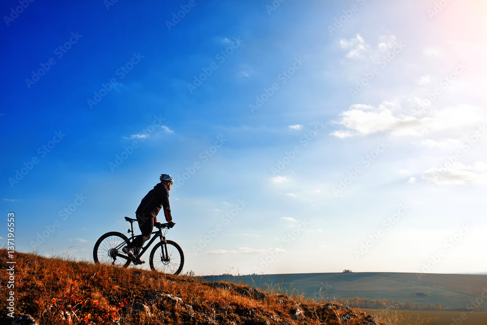 Cyclist riding his bike down on mountain trail. Beautiful sky and clouds on background
