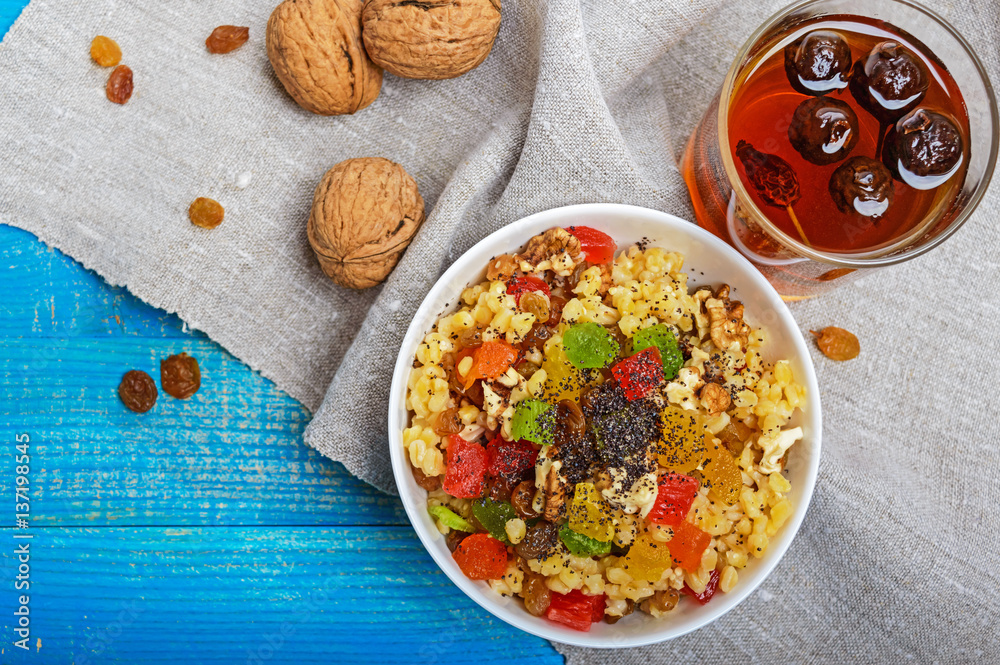 Diet fitness wheat porridge with nuts, raisins, slices of citrus fruit (grapefruit, orange, kiwi), poppy seeds, honey, in a white bowl on a blue wooden background. The top view. Diet fitness wheat porridge with nuts, raisins, slices of citrus fruit (grapefruit, orange, kiwi), poppy seeds, honey, in a white bowl on a blue wooden background. The top view.