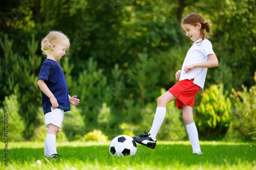 Two cute little sisters having fun playing a soccer game