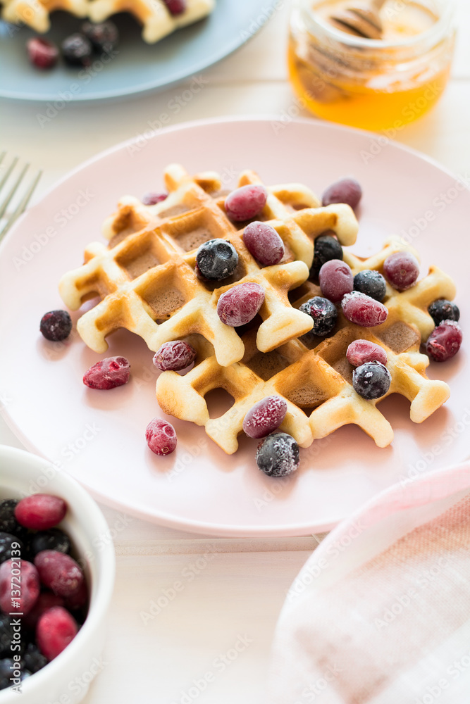 Belgian waffles with honey and frozen berries on white wooden table. Selective focus Belgian waffles with honey and frozen berries on white wooden table. Selective focus