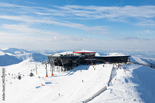 modern cableway skiing resort in austrian alps with skiers and snowboarders on blue sky mountain peak 