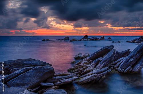 Sunrise over lake Malawi with rock formation in the foreground under cloudy dramatic sky