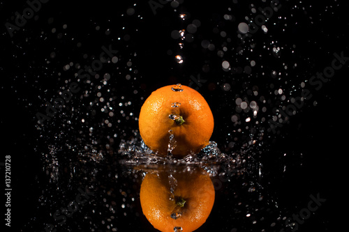 Sparkling water falls on juicy red orange which stands on black table