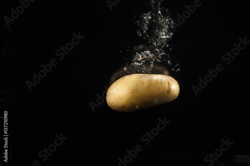 Delicious raw potato sinks in water on black background photo