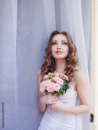 Gorgeous bride with deep blue eyes looks up posing before white curtains
