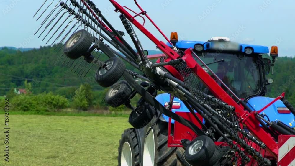 One side of the machinery slowly lowers down until it touches the ground. It is a nice summer day out in the fields.
