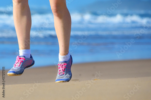 Fitness and running on beach, woman runner legs in shoes on sand near sea, healthy lifestyle and sport concept 