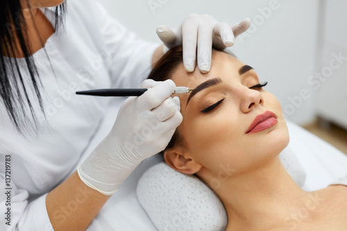 Beautician Doing Permanent Eyebrows Makeup Tattoo On Woman Face photo