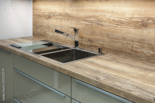 Modern designer chrome water tap over stainless steel kitchen sink on the table top made of natural wood