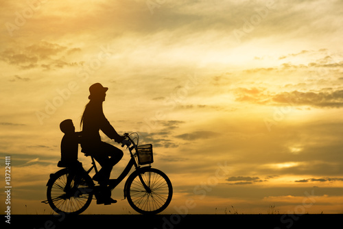 Silhouette of mother and child,cycling togetherThe background image is a sunset in Thailand