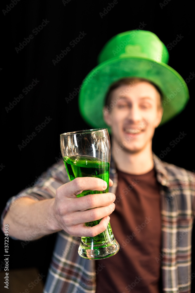 smiling man holding glass of beer in hand on St.Patrick's day on black