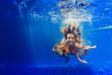 Happy family - mother, baby son, daughter swim and dive in pool with fun - jump deep down underwater with splashes. Lifestyle, summer children water sports activity and swimming lessons with parents.