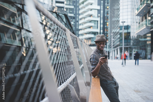 young handsome afro black man sitting on a handrail outdoorusing smart phone - technology, social network, communication concept