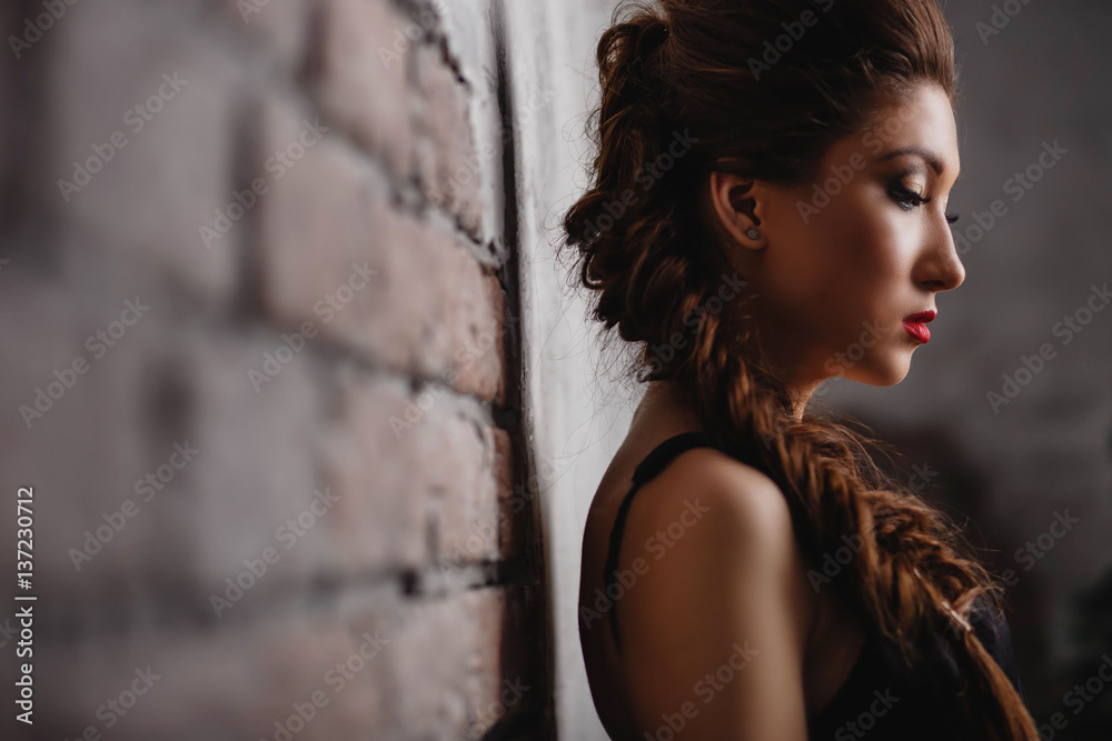 beautiful girl with bright makeup wearing a black dress with pigtails looking down on a light brick background closeup