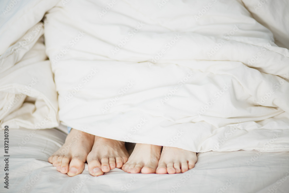 the legs of two lovers men and women girl and boy stick pop out under the white soft fluffy clean blanket on the bed the foreground white background the legs of two lovers men and women girl and boy stick pop out under the white soft fluffy clean blanket on the bed the foreground white background